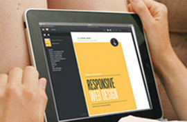 Close up shot of a tablet in someones lap; on the screen there is a yellow webpage that says: Responsive web design.